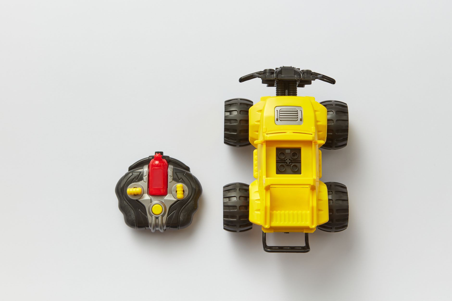Overhead view of a yellow remote-controlled toy car with its controller on a white background.