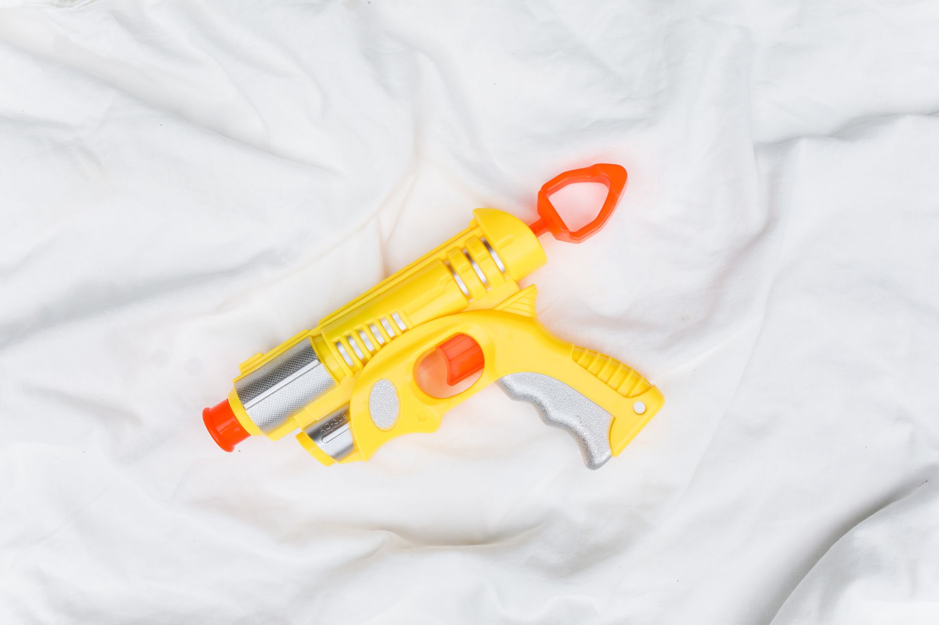 A vibrant yellow toy water gun with red accents placed on white fabric background.