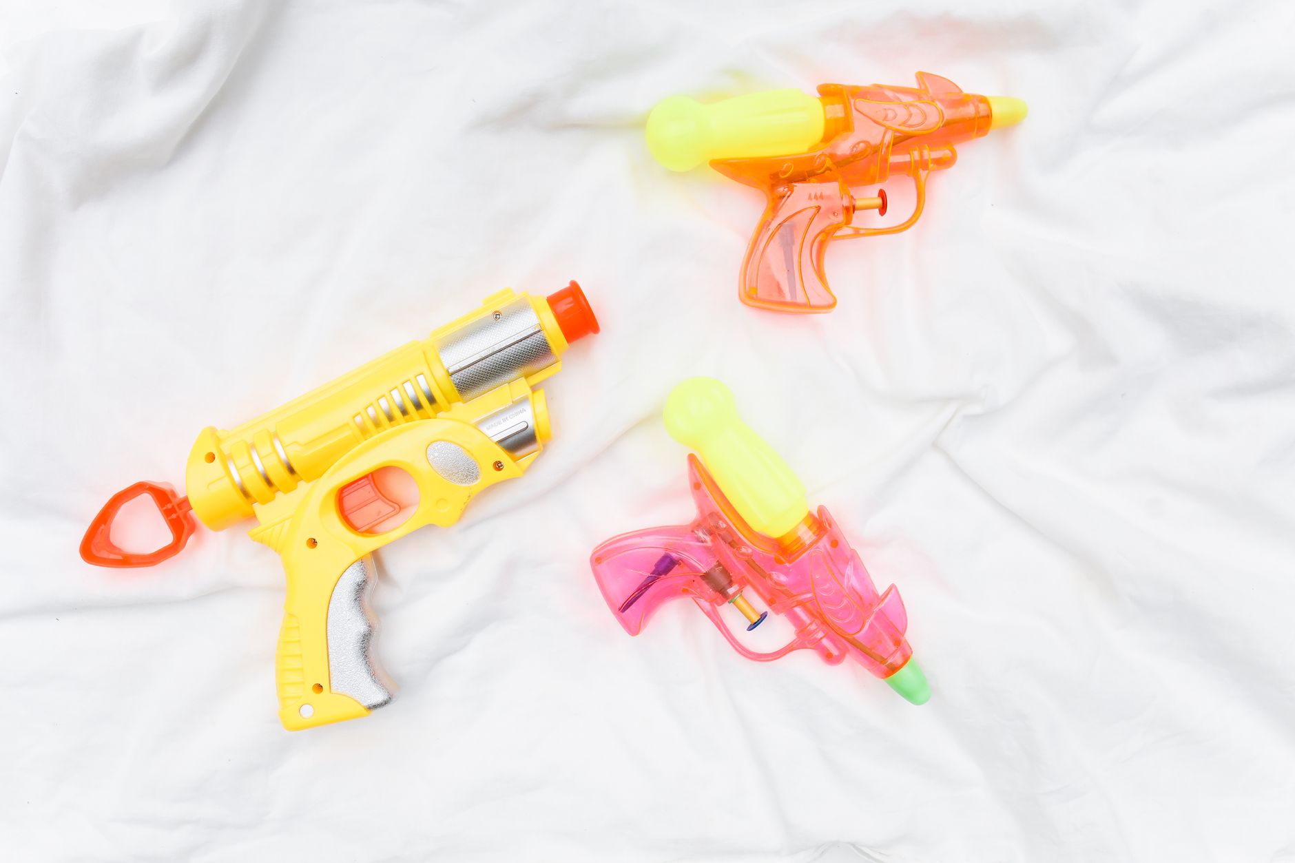 Vibrant plastic water guns placed on a soft white surface.