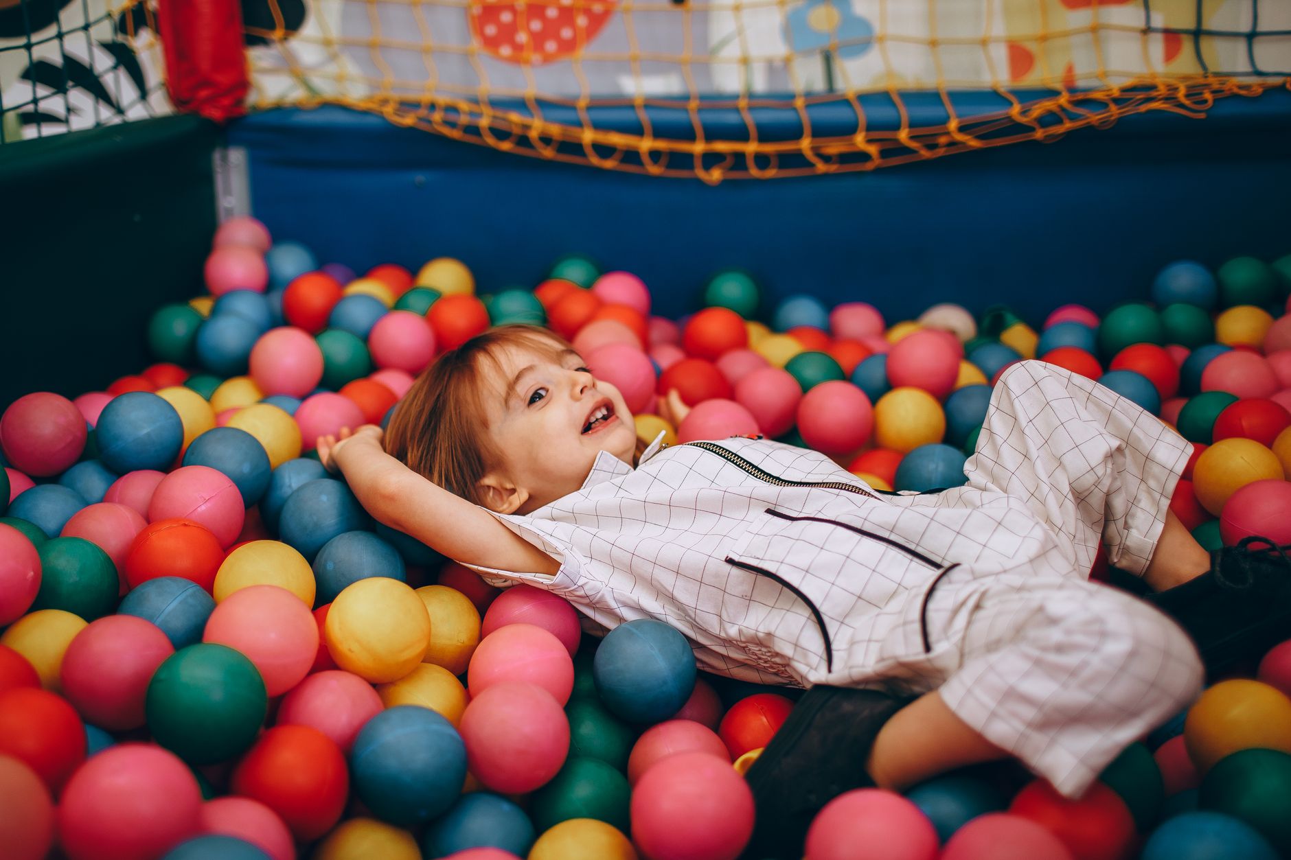 A joyful child playing in a vibrant ball pit full of colorful balls, indoors.