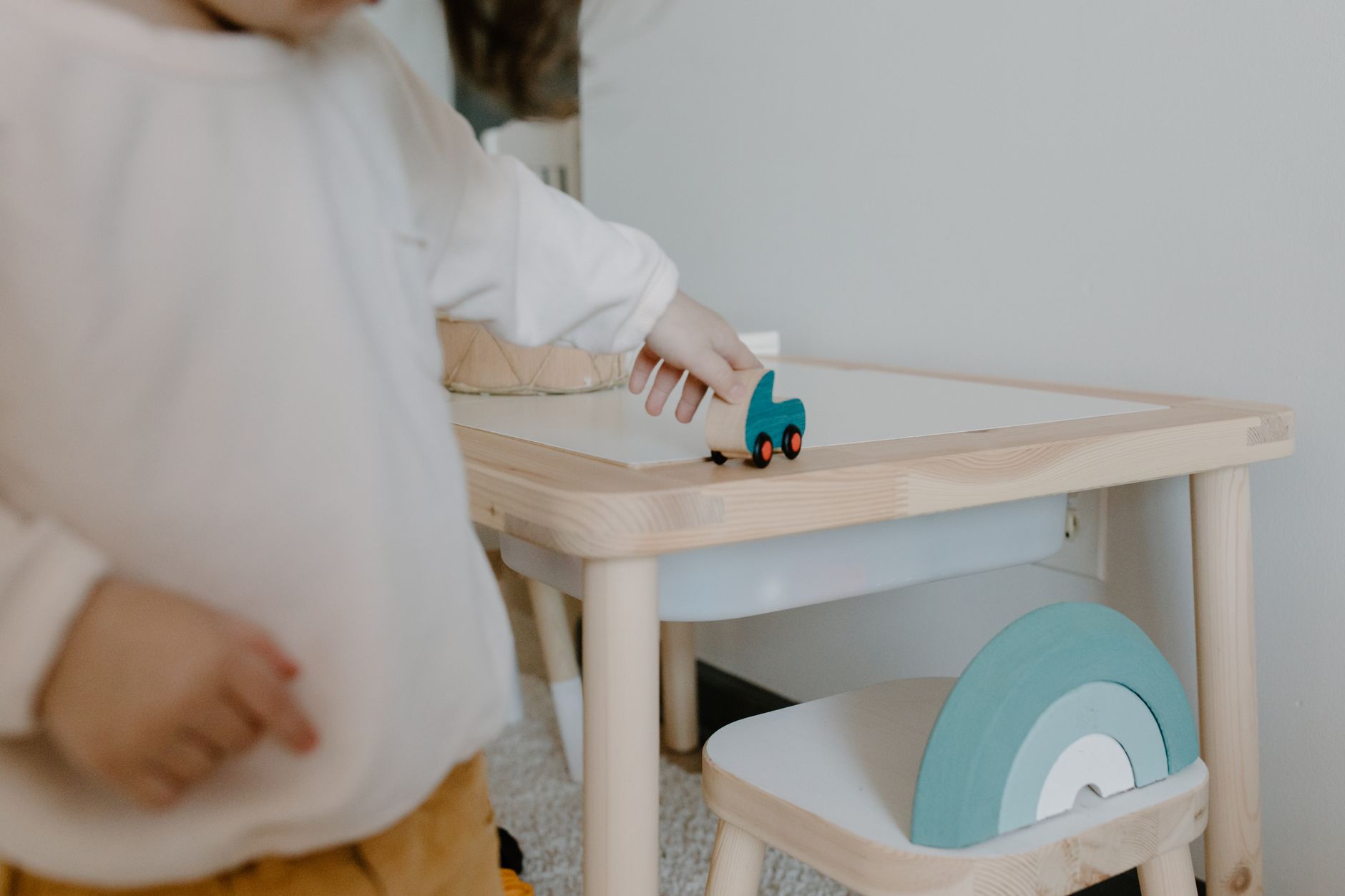 A young child plays with a wooden toy on a small table indoors, showcasing minimalist design.