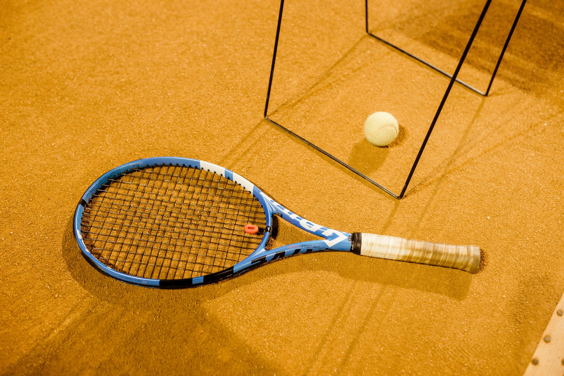 Close-up of a blue tennis racket and ball on an indoor clay court, perfect for sports imagery.