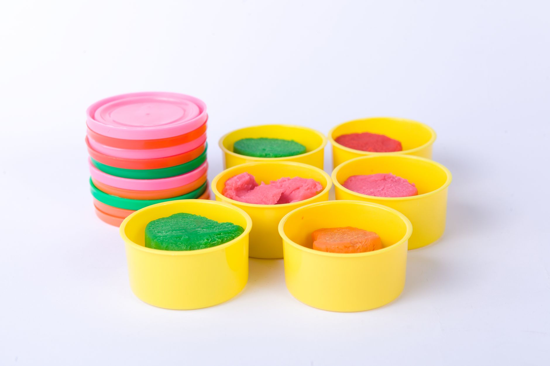 Colorful playdough in yellow containers with stacked pastel lids on white background.