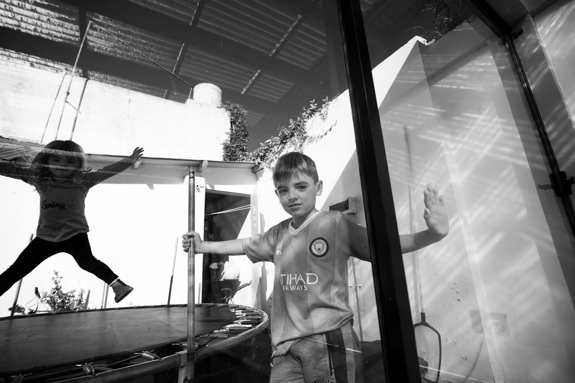 Children playing on a trampoline indoors in black and white setting.