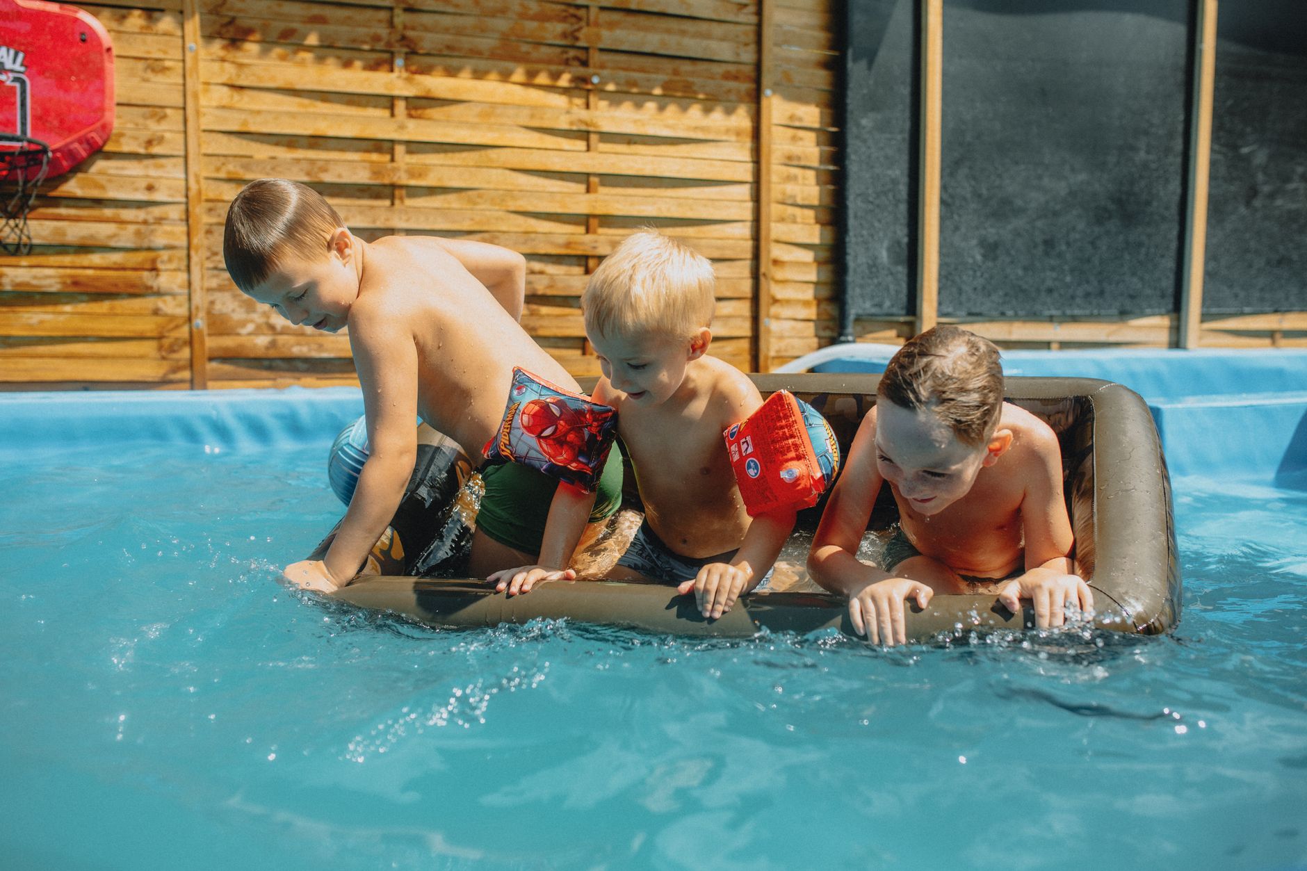 Three children playing in a pool with inflatables on a sunny summer day.