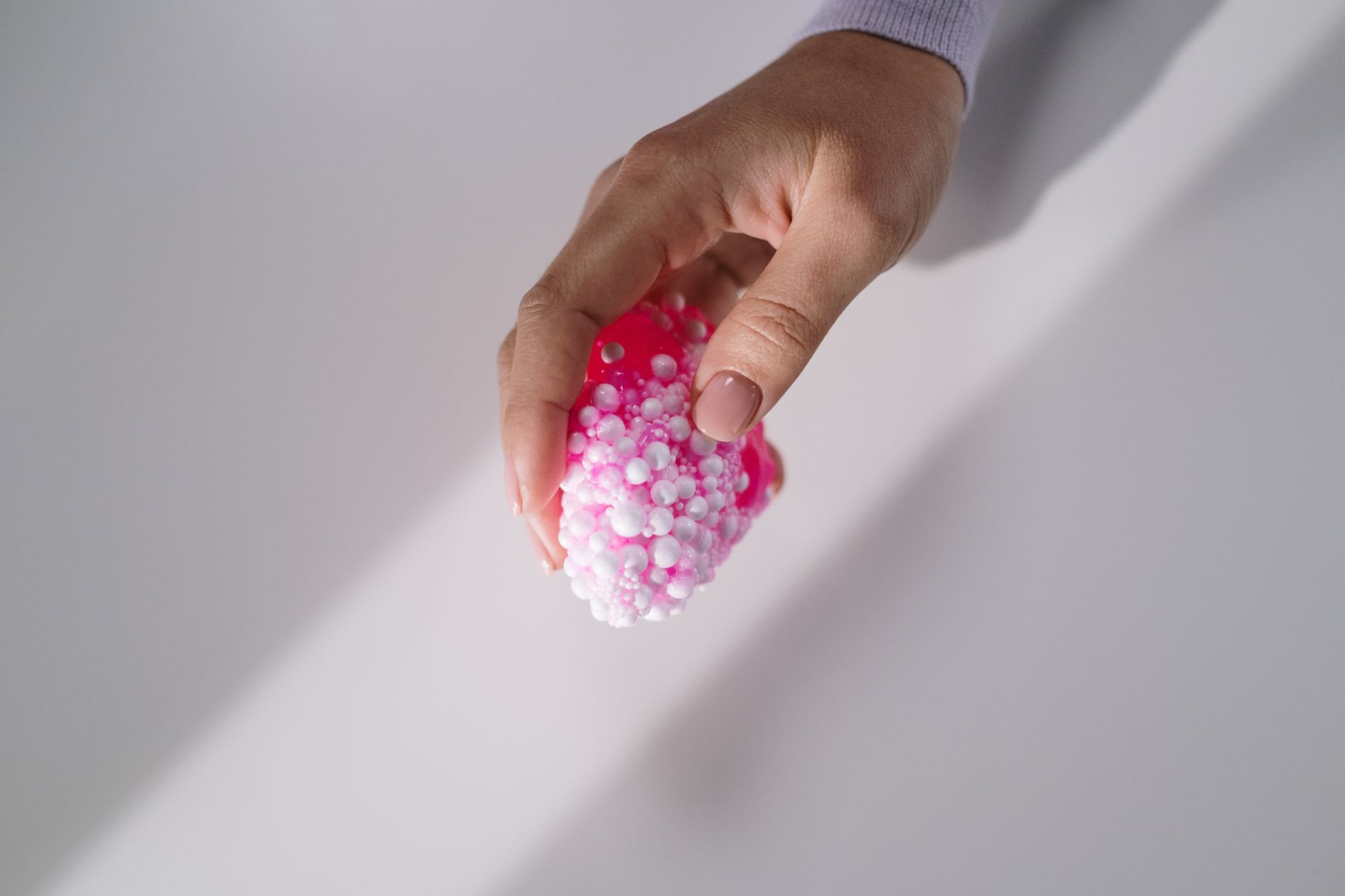 A hand gently holds a pink textured slime with small foam beads, showcasing tactile sensation.