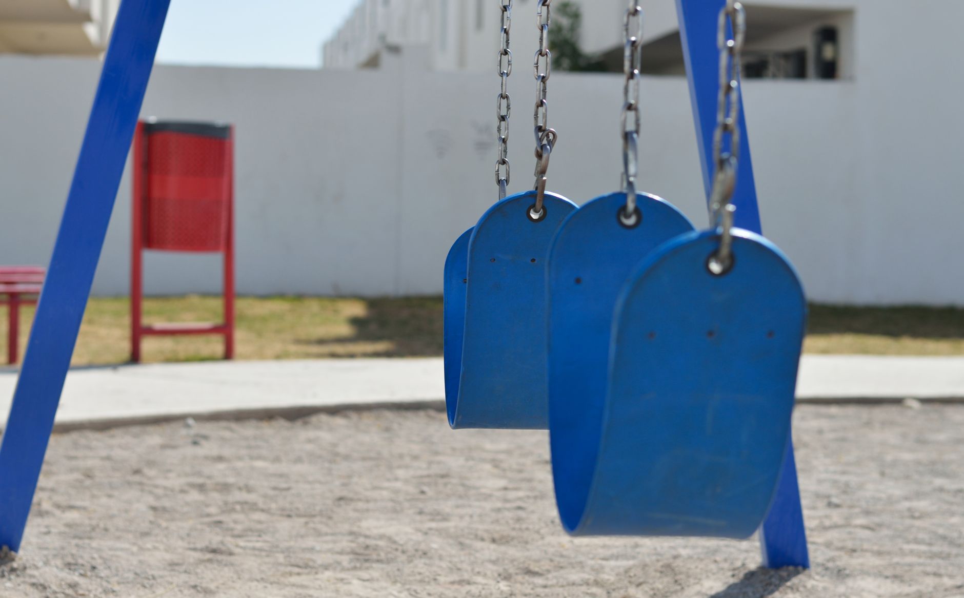 Blue swings in a sunny outdoor playground with sand and grass.