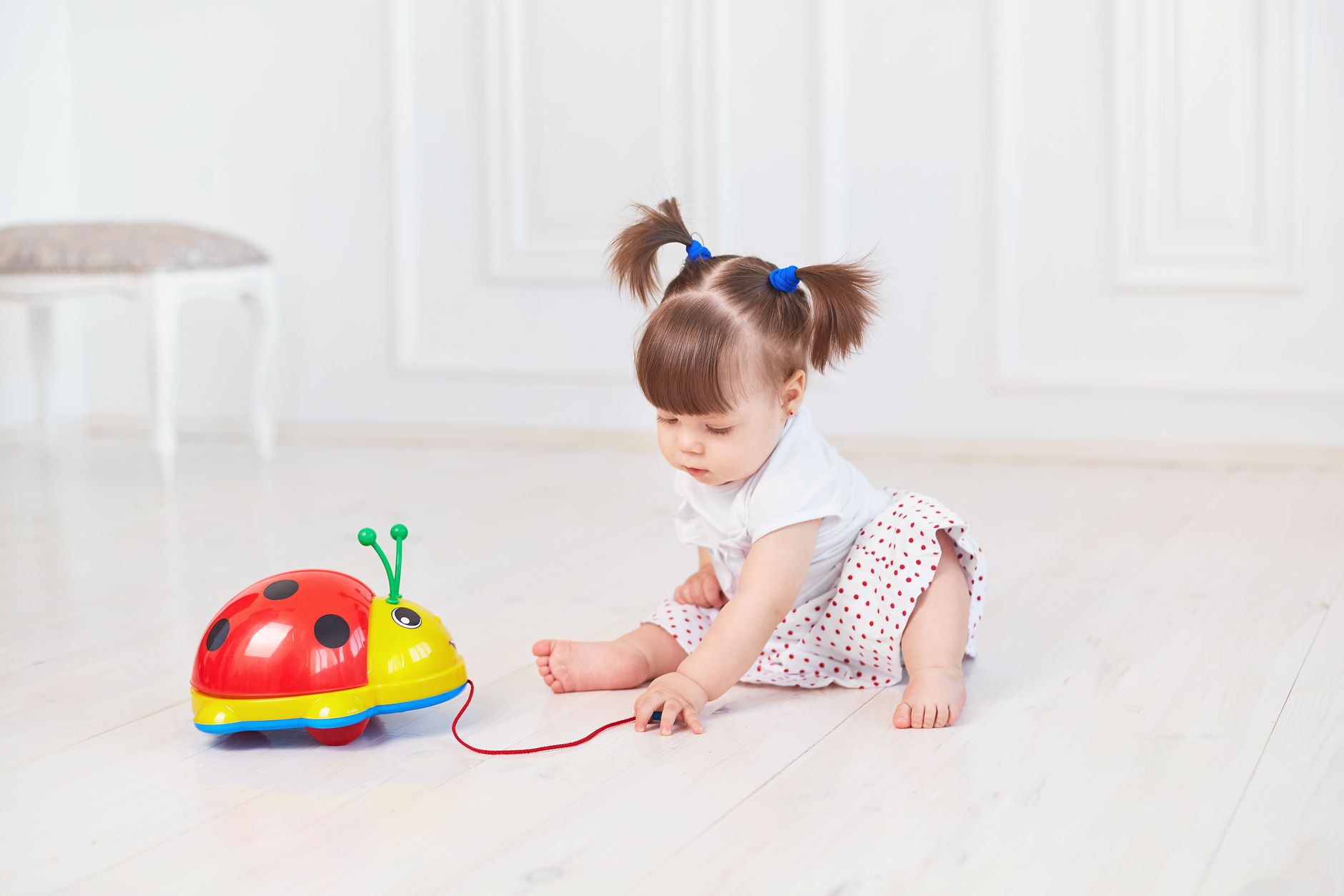 Cute toddler sits on the floor playing with a colorful toy ladybug.