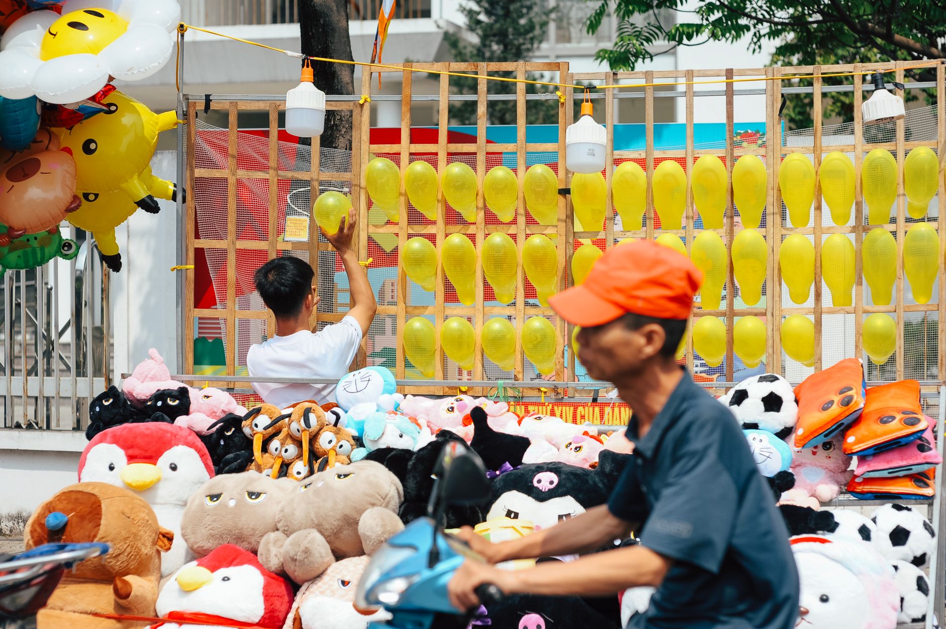 Street vendor setting up a colorful outdoor stall with yellow balloons and plush toys.
