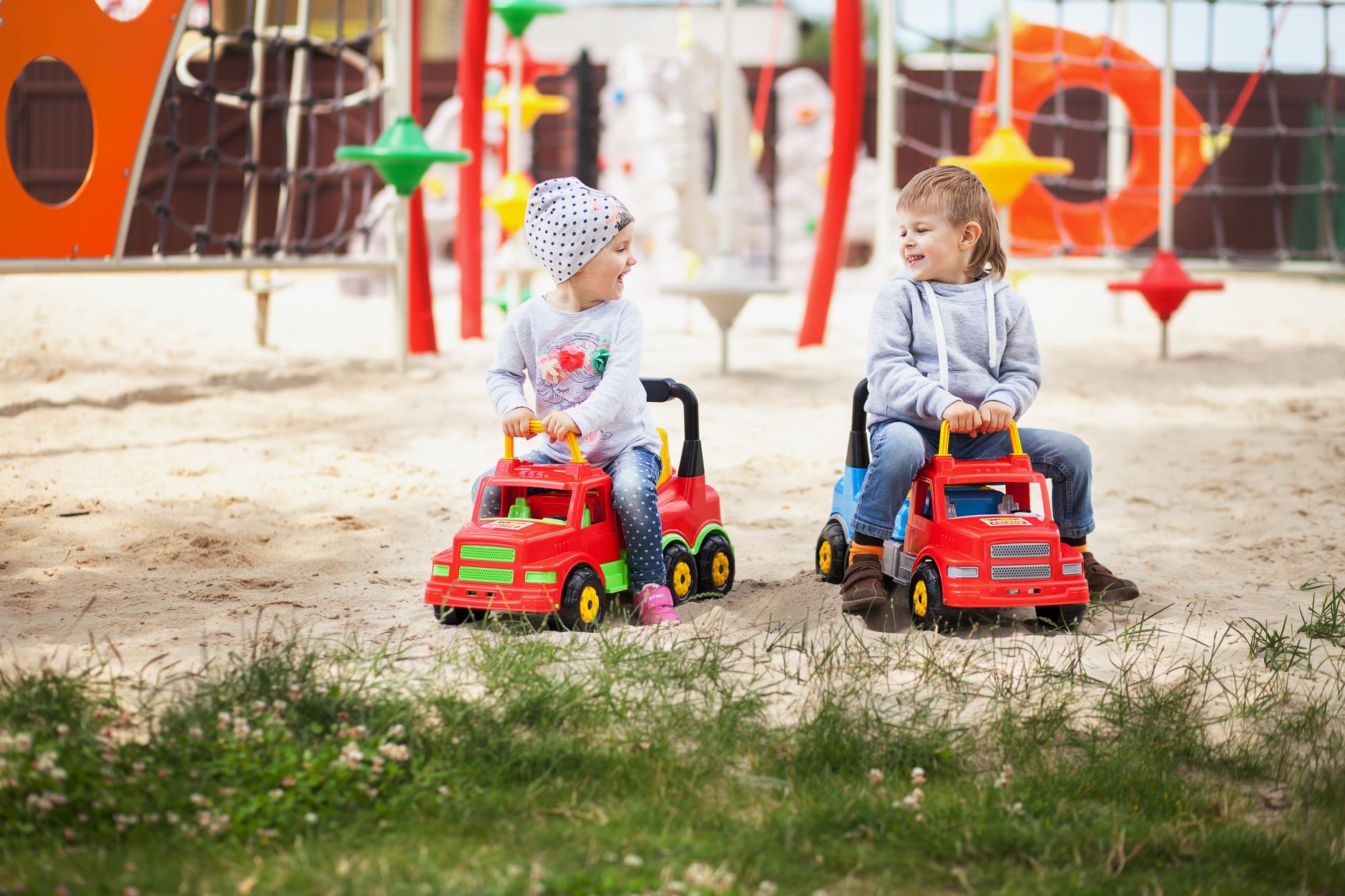 Two children enjoying outdoor play with plastic toy trucks in a playground sandbox.