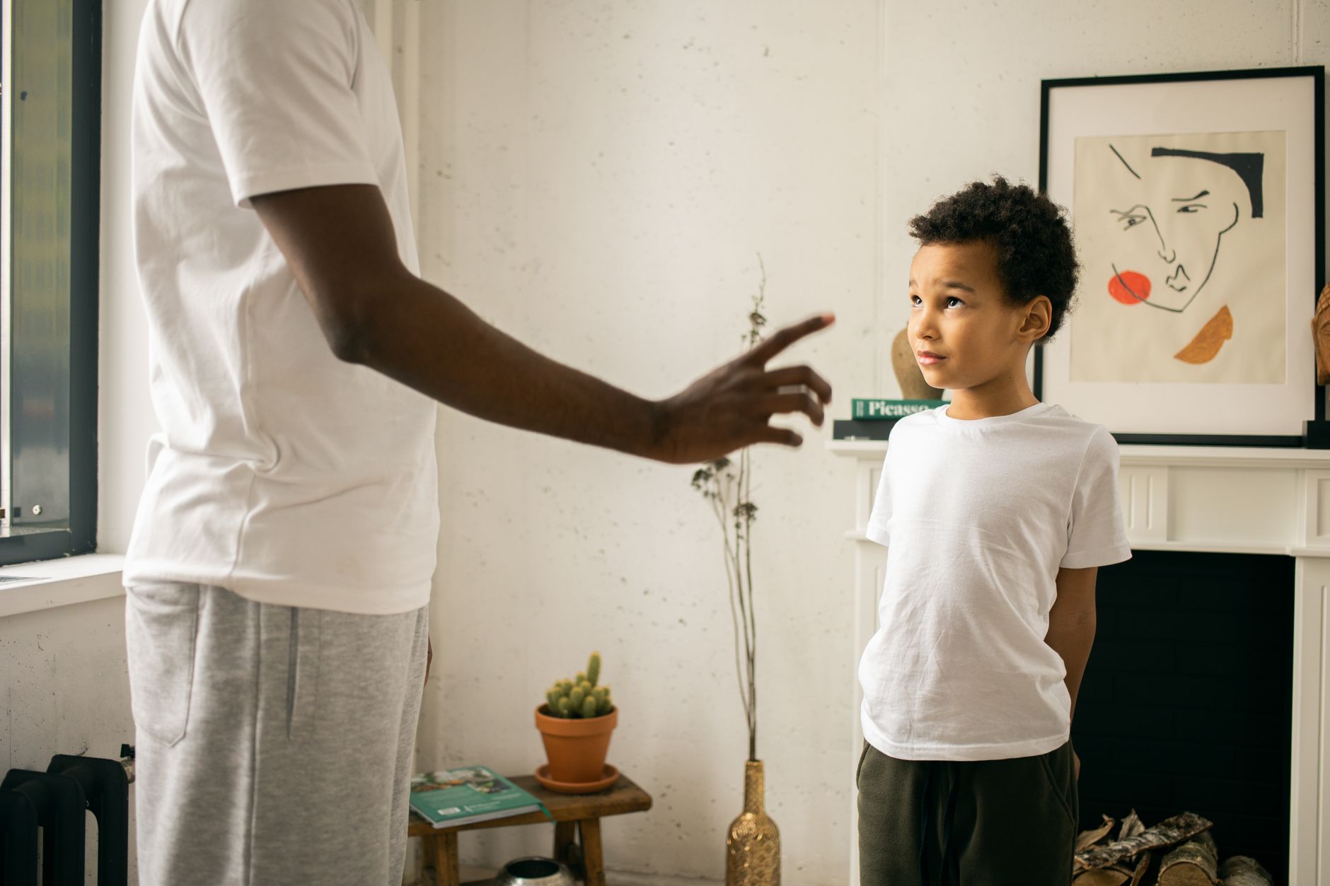 Crop unrecognizable African American father pointing finger and explaining behavior rules to cute guilty son in modern apartment