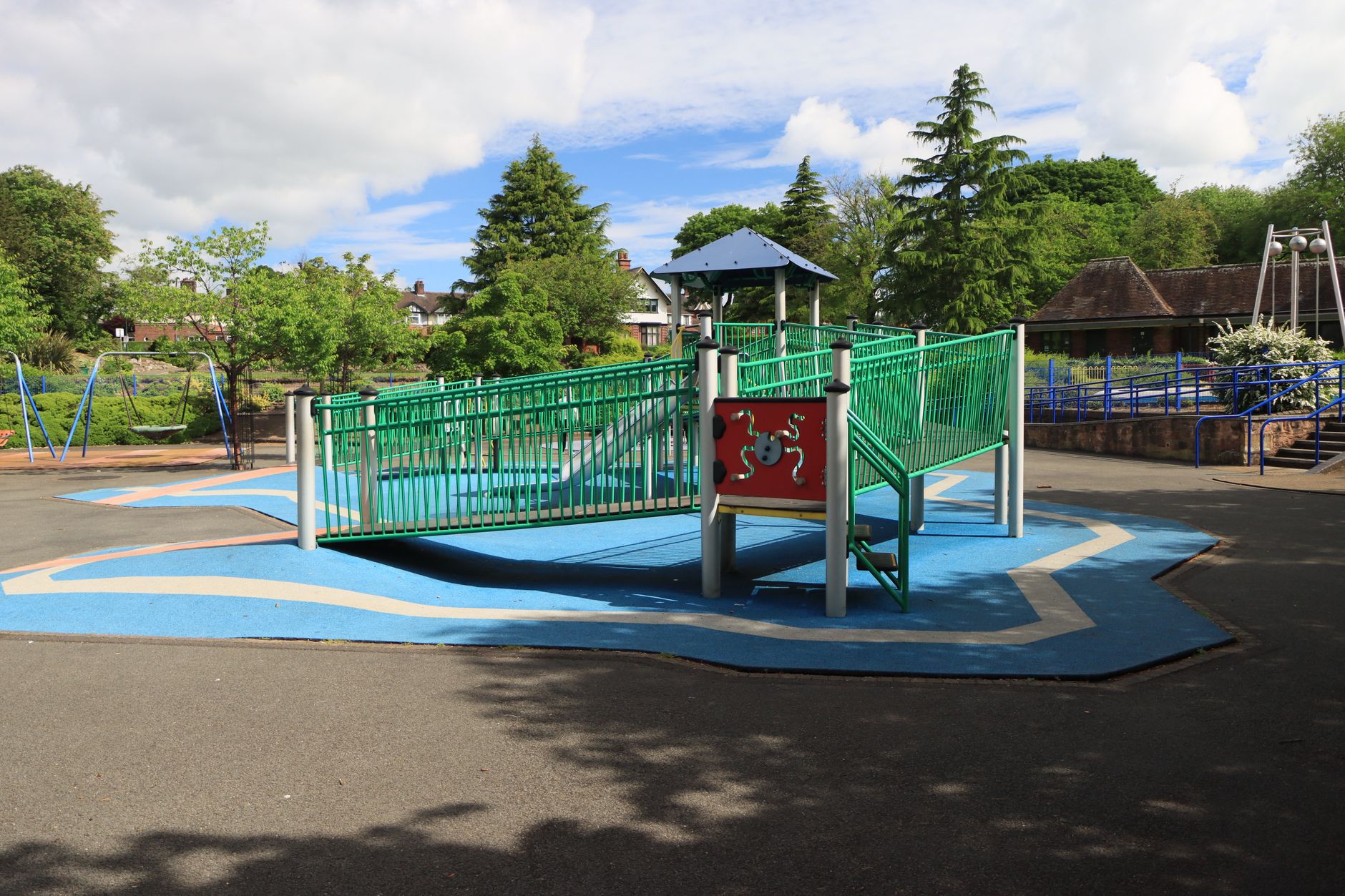 A colorful playground with slides and swings in a sunlit park surrounded by greenery.