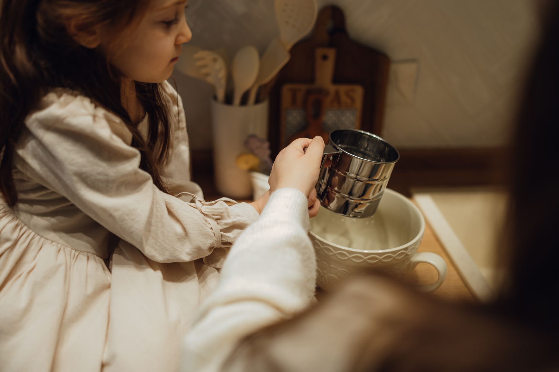 A young girl assisting with kitchen tasks, using a measuring cup in a warm, cozy setting.