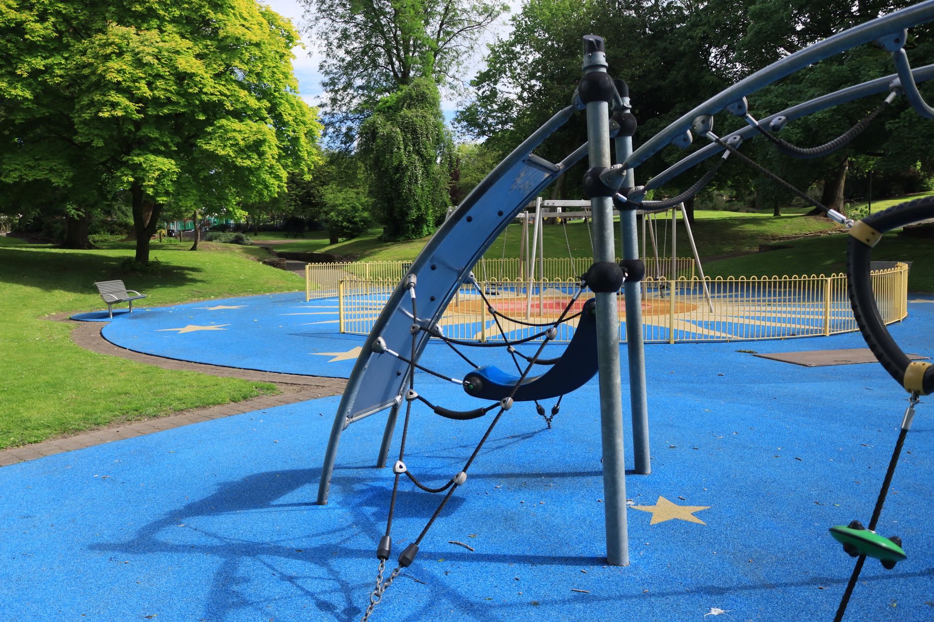 A vibrant playground with blue rubber flooring and climbing structures in a lush green park.