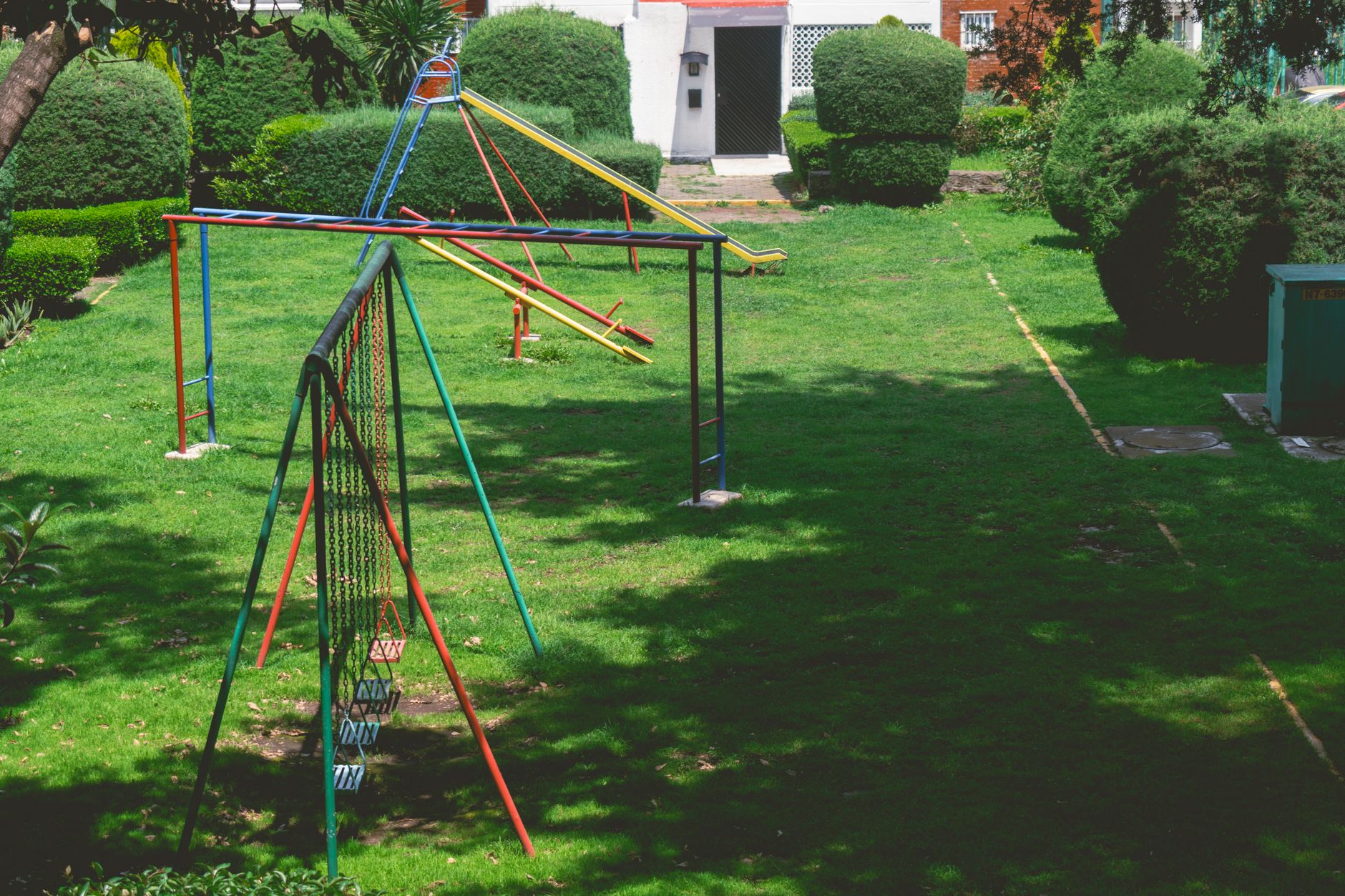 Vibrant outdoor playground with swings and slides in a lush green park setting under a bright sky.
