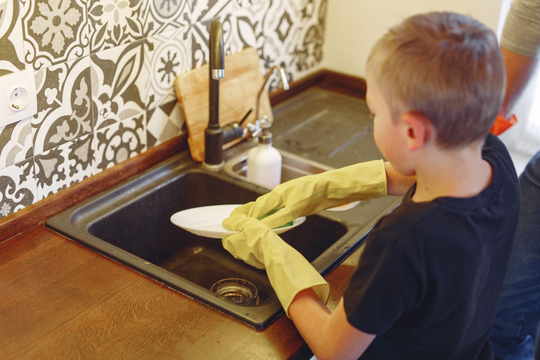 From above of small focused boy diligently dishwashing at kitchen under father supervision