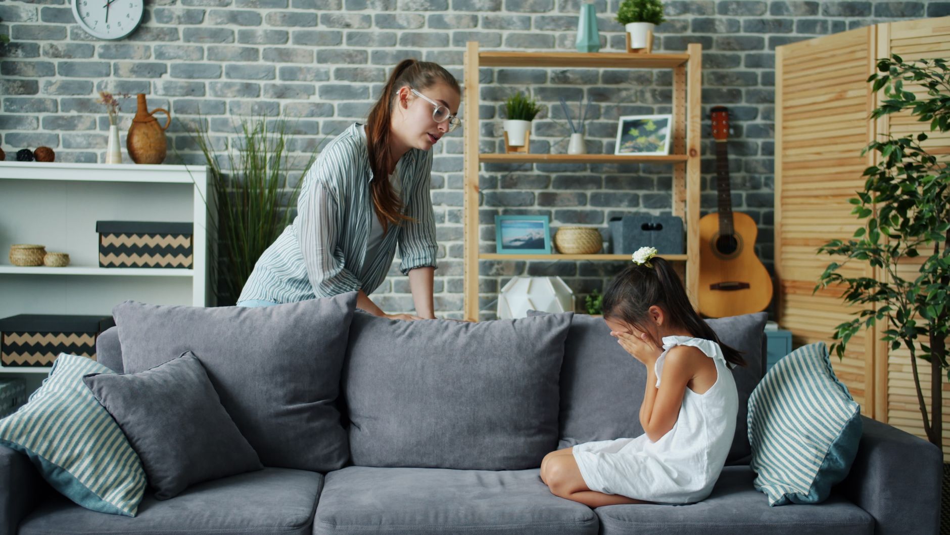 A mother comforts her crying daughter in a cozy living room setting.