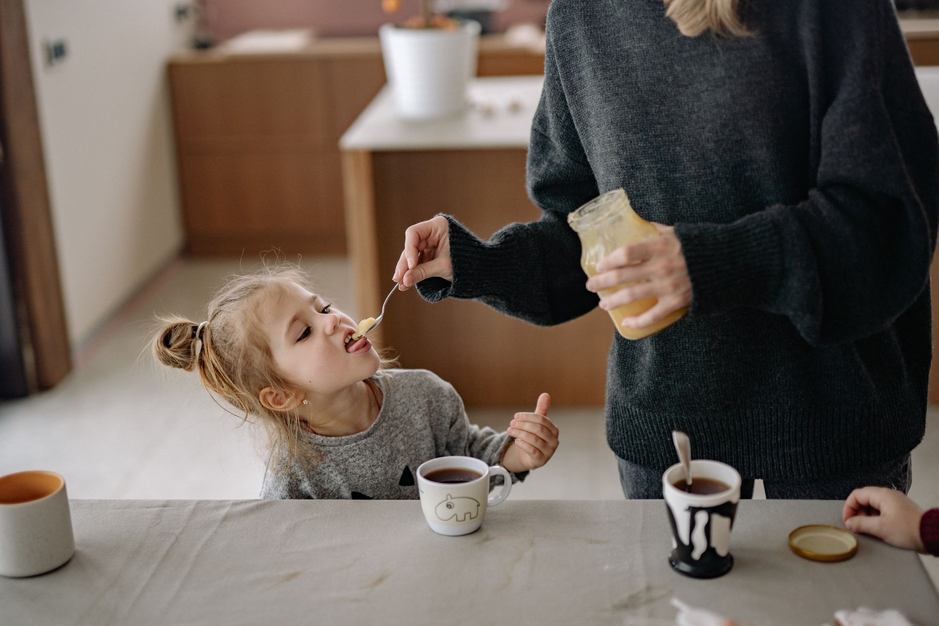 A child enjoys honey during a warm and cozy family breakfast with tea.