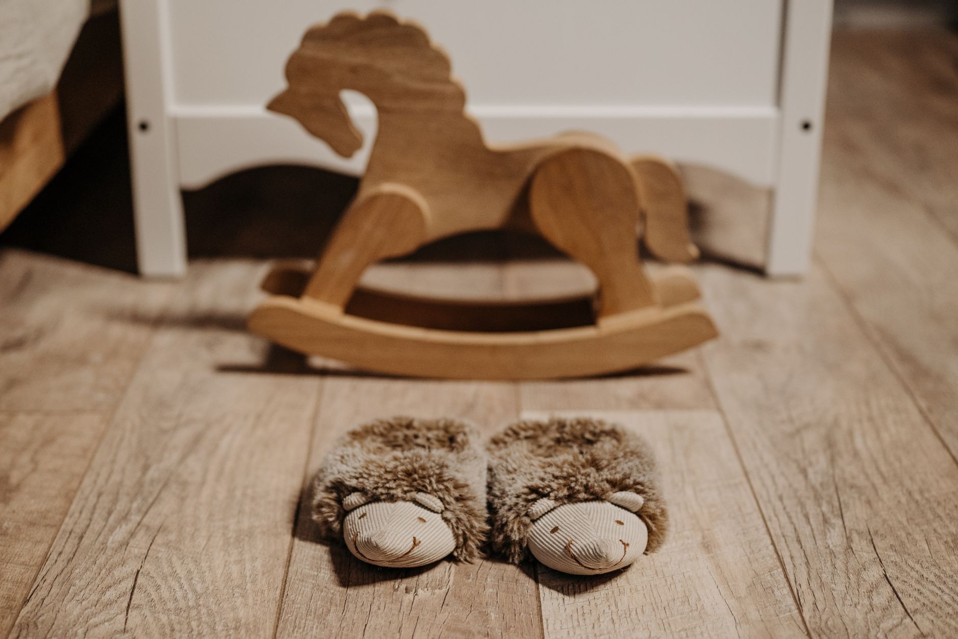 Warm, fluffy slippers on wooden floor in nursery beside a wooden rocking horse.